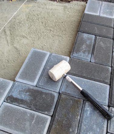 A white rubber mallet lies on the surface of a gray Brick paving slab. Tools and materials for paving works. Beautiful building background with copy space